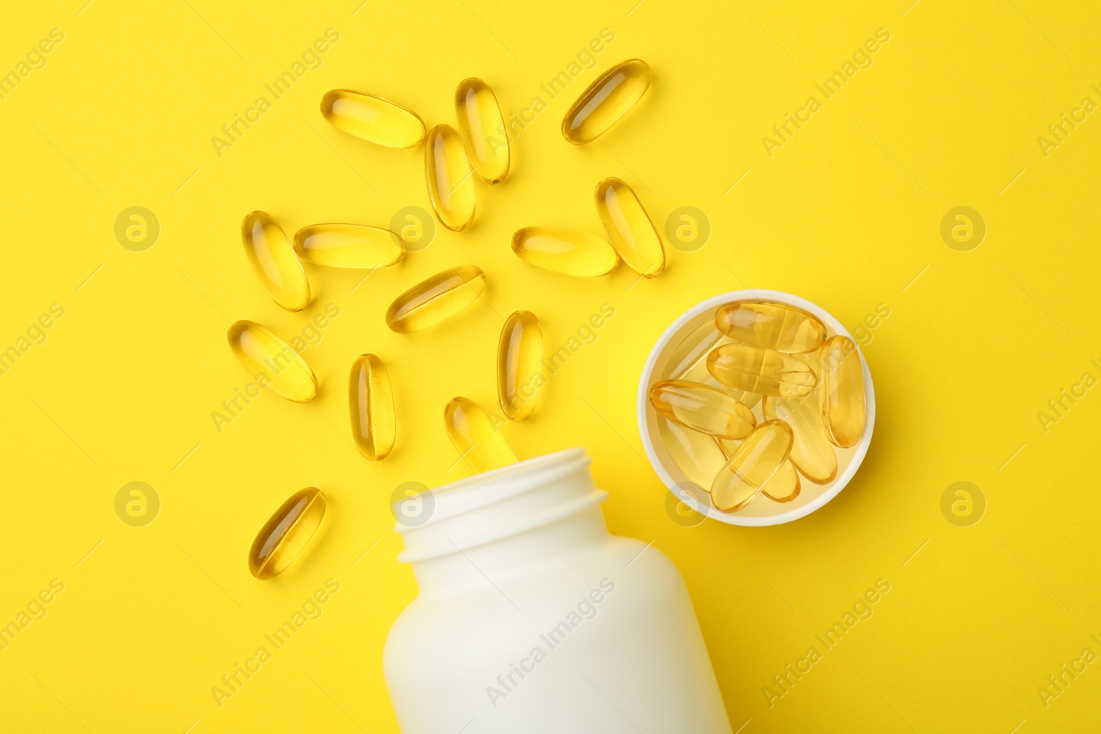 Photo of Softgel capsules, lid and bottle on yellow background, flat lay