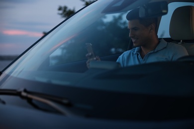 Handsome man with smartphone in modern car, view from outside