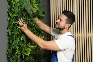 Man installing green artificial plant panel on grey wall in room