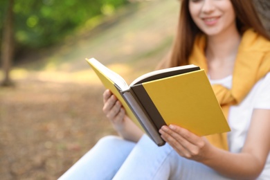 Photo of Young woman reading book outdoors, closeup view