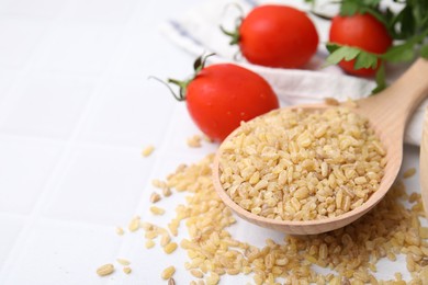 Photo of Spoon with raw bulgur and tomatoes on table, closeup. Space for text