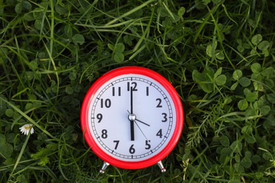 Photo of Red alarm clock on green grass outdoors, top view. Space for text