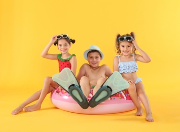 Cute little children in beachwear with bright inflatable ring on yellow background