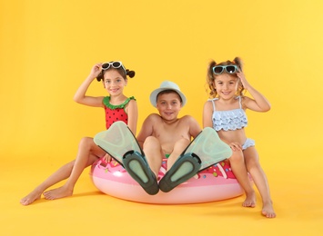 Photo of Cute little children in beachwear with bright inflatable ring on yellow background