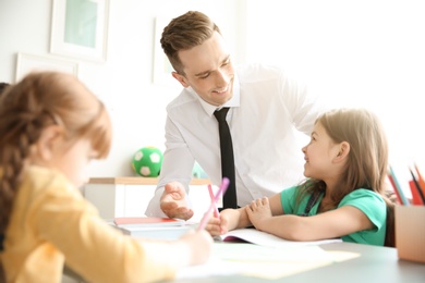 Male teacher helping girl with her task in classroom at school