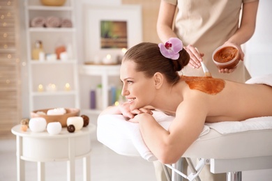 Beautiful young woman having massage with body scrub in spa salon