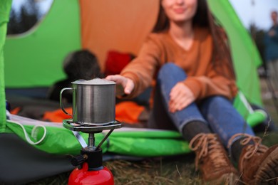 Photo of Woman taking cup off stove while sitting in camping tent outdoors, closeup