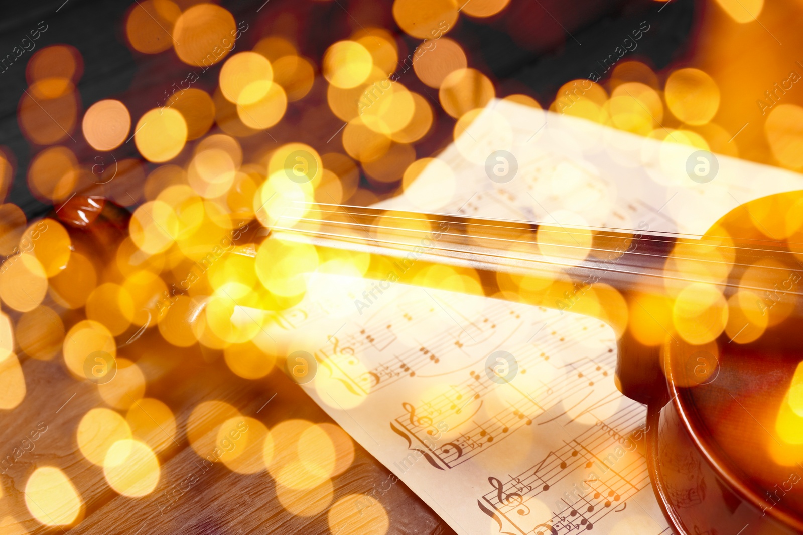 Image of Christmas and New Year music. Violin and music sheets on wooden background, bokeh effect