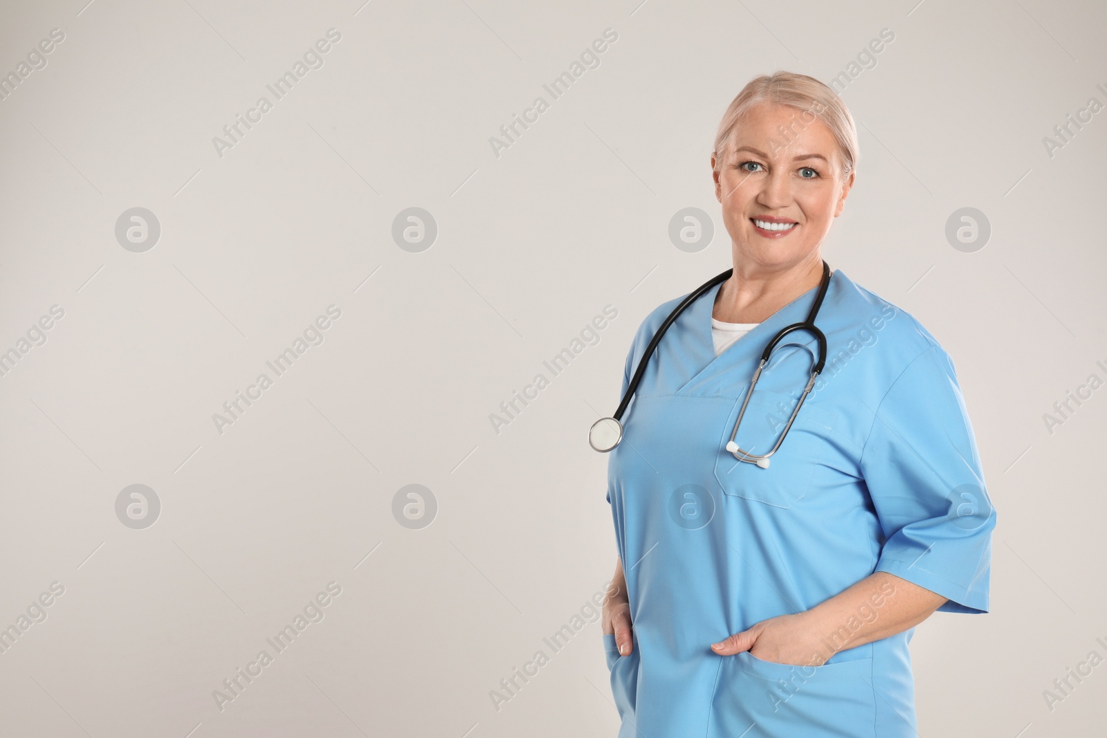 Photo of Portrait of mature doctor with stethoscope on light grey background. Space for text