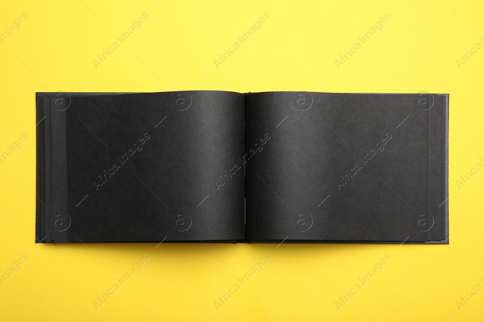 Photo of Stylish open black notebook on yellow background, top view