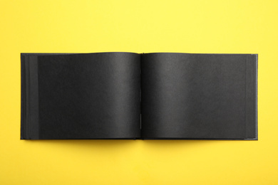 Photo of Stylish open black notebook on yellow background, top view