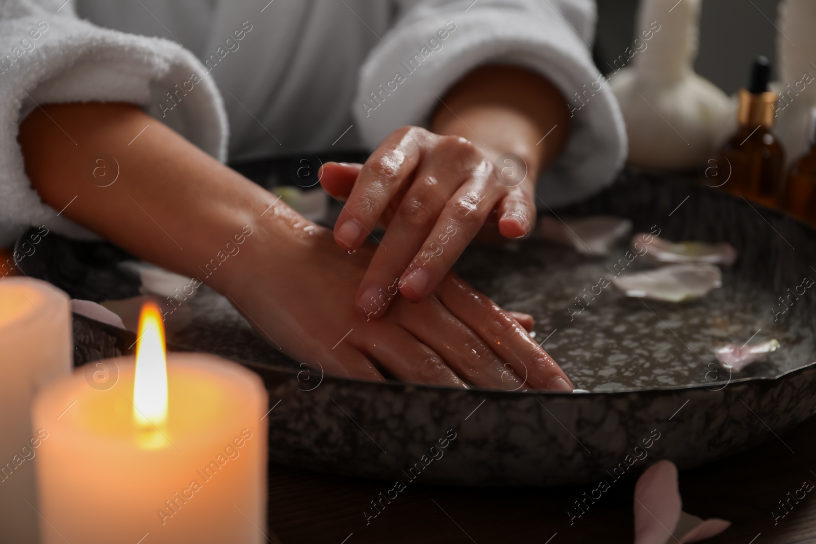 Photo of Woman soaking her hands in bowl of water and flower petals, closeup. Spa treatment