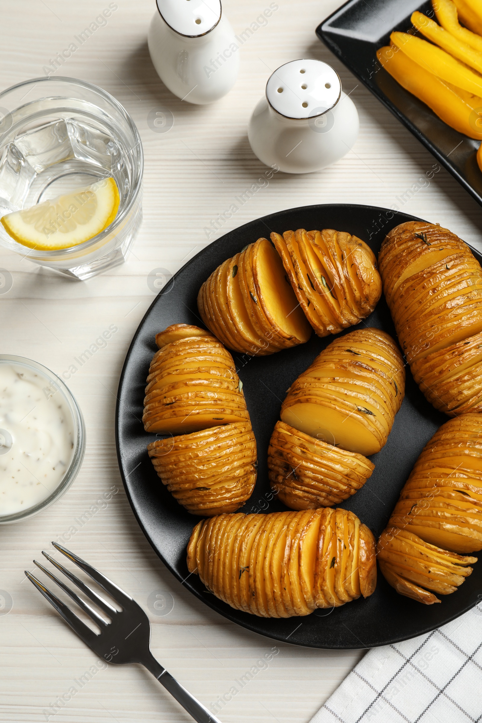 Photo of Delicious homemade Hasselback potatoes served on white wooden table, flat lay