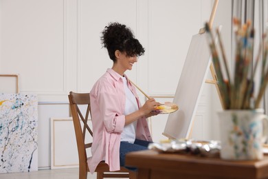 Young woman mixing paints on palette with brush near easel in studio