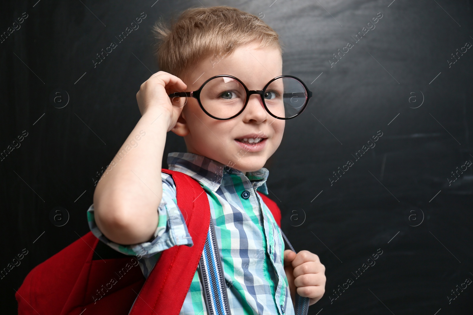 Photo of Cute little child wearing glasses near chalkboard. First time at school