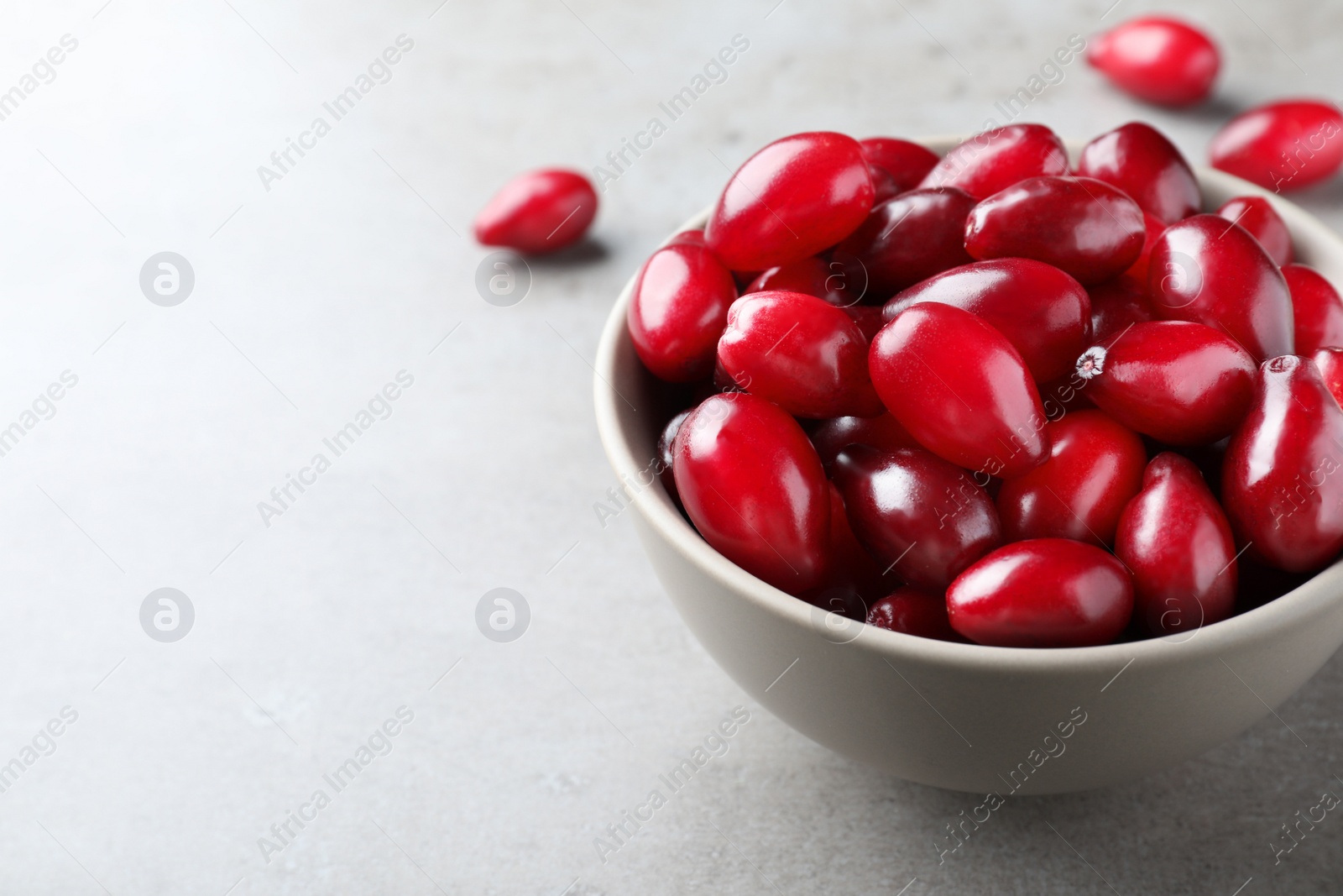 Photo of Fresh ripe dogwood berries in bowl on light grey table, closeup. Space for text