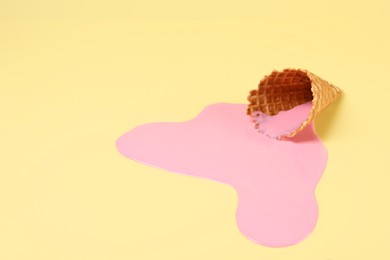 Photo of Melted ice cream and wafer cone on pale yellow background, space for text