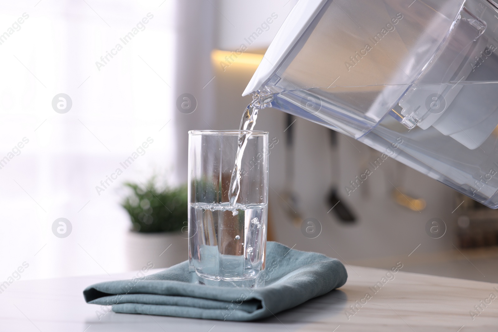 Photo of Pouring water from filter jug into glass in kitchen, closeup