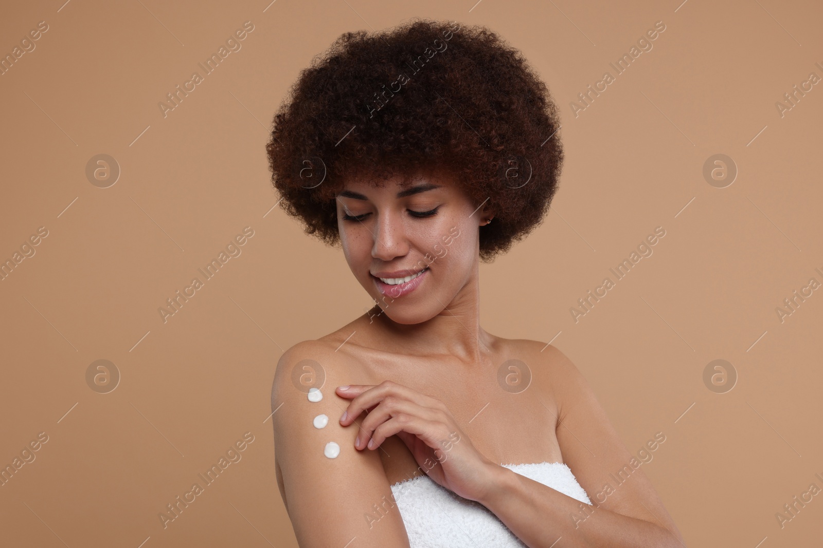 Photo of Beautiful young woman applying body cream onto arm on beige background