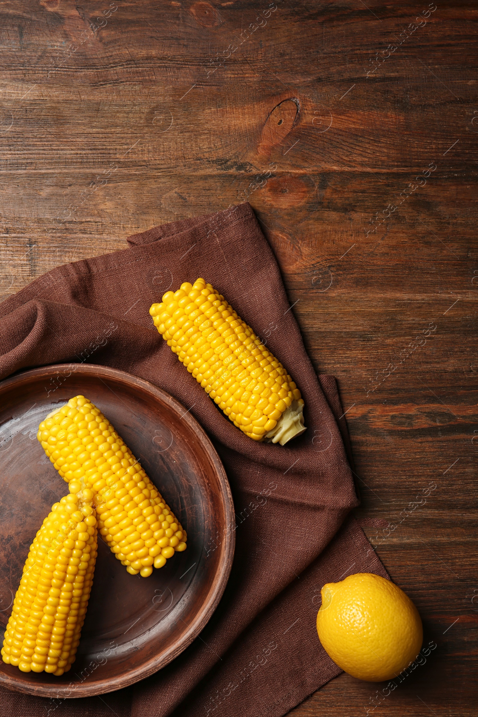 Photo of Flat lay composition with corn cobs and lemon on wooden background. Space for text