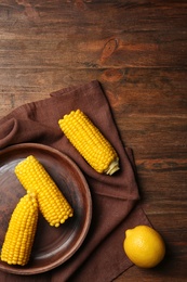 Flat lay composition with corn cobs and lemon on wooden background. Space for text