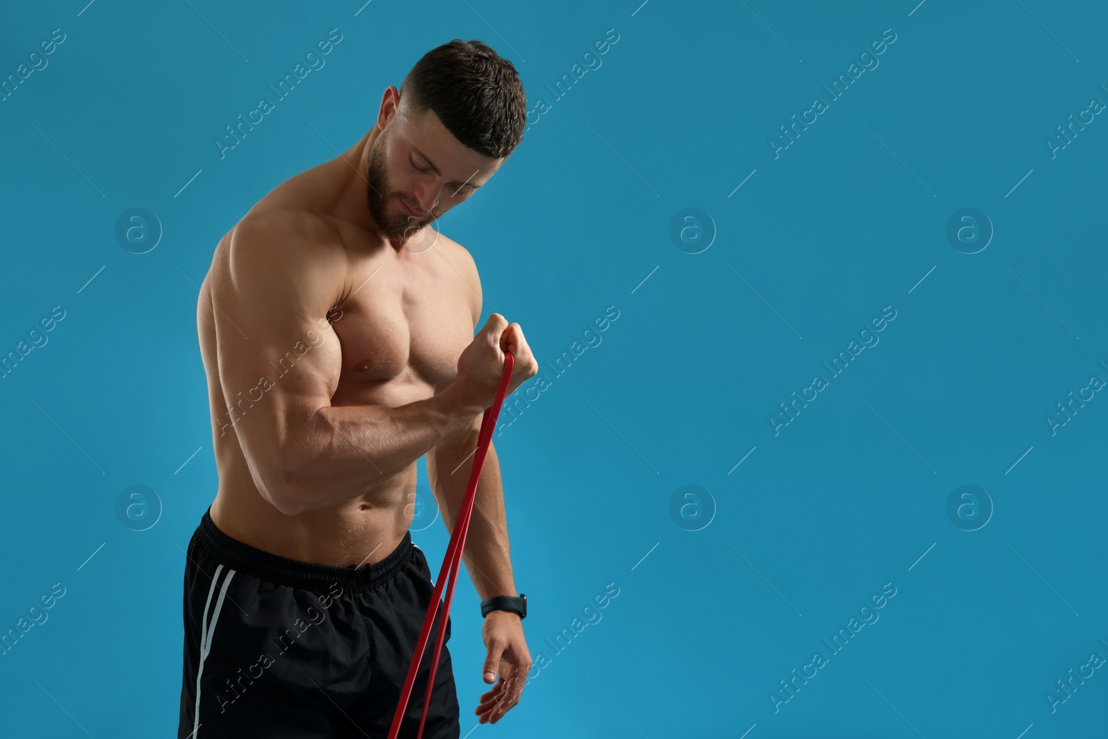 Photo of Muscular man exercising with elastic resistance band on light blue background. Space for text