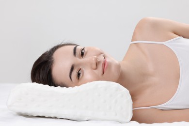 Woman lying on orthopedic pillow against light grey background