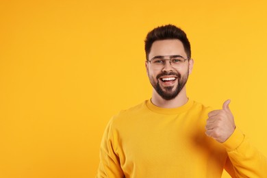 Photo of Handsome man in glasses showing thumbs up on orange background, space for text