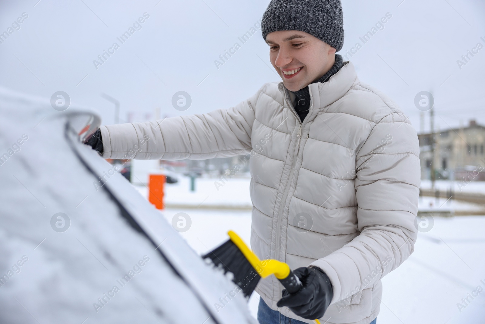 Photo of Man cleaning snow from car with brush outdoors