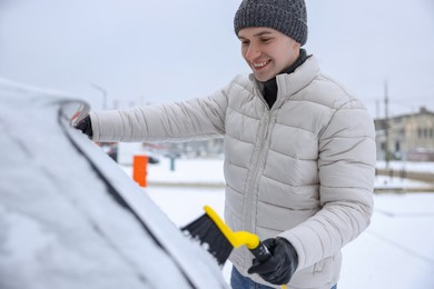 Man cleaning snow from car with brush outdoors