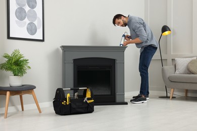 Photo of Man sealing electric fireplace with caulk near wall in room
