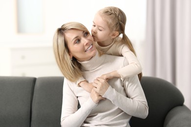 Photo of Daughter kissing her happy mother on sofa at home