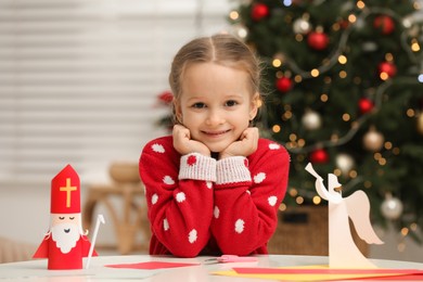 Photo of Cute little girl with paper Saint Nicholas and angel toys at home