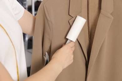 Photo of Woman using adhesive lint roller indoors, closeup. Dry-cleaning service