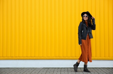 Photo of Beautiful young woman in stylish autumn clothes near yellow fence. Space for text