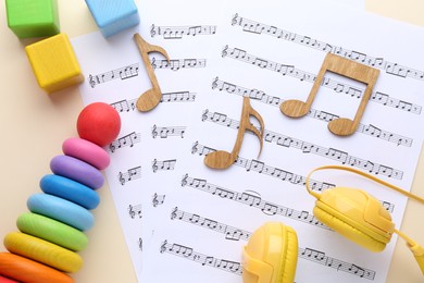 Photo of Wooden notes, music sheets, headphones and toys on beige background, flat lay. Baby song concept