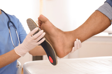 Photo of Female orthopedist fitting insole on patient's foot in clinic, closeup