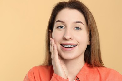 Portrait of smiling woman with dental braces on beige background, closeup