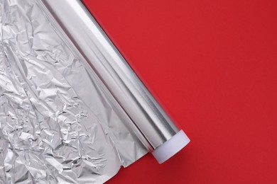 Photo of Roll of aluminum foil on red background, top view. Space for text