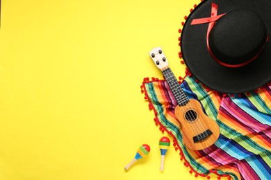 Photo of Mexican sombrero hat, guitar, maracas and colorful poncho on yellow background, flat lay. Space for text