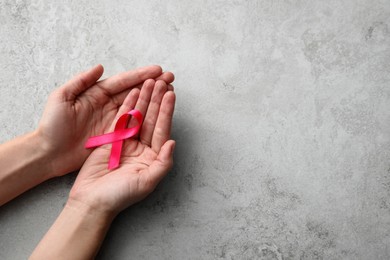 Photo of Woman holding pink ribbon at grey table, top view with space for text. Breast cancer awareness concept