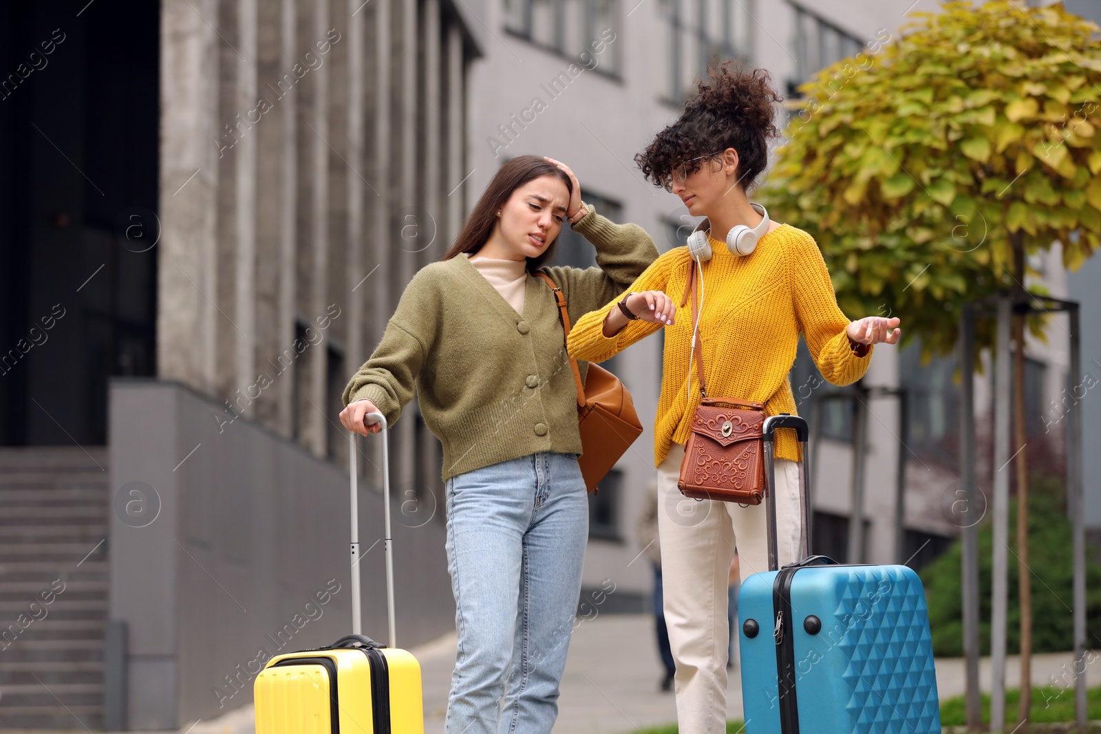 Photo of Being late. Worried women with suitcases looking at watch outdoors