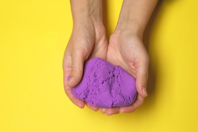 Woman playing with kinetic sand on yellow background, top view