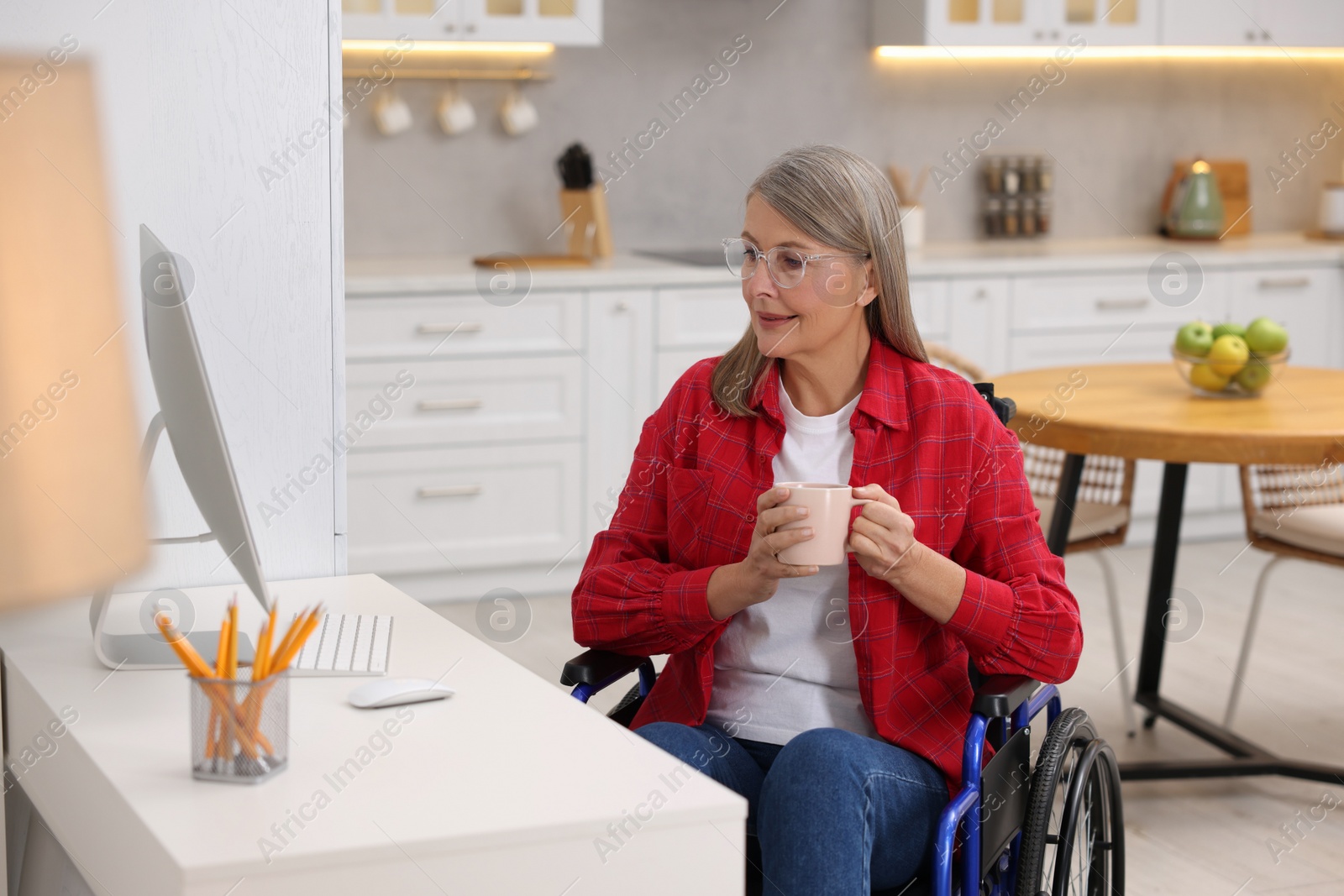 Photo of Woman in wheelchair with cup of drink using computer at home