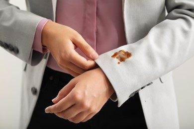 Woman showing stain of coffee on her jacket against white background, closeup