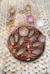 Photo of Beautiful Christmas tree baubles and fairy lights on white knitted fabric, above view