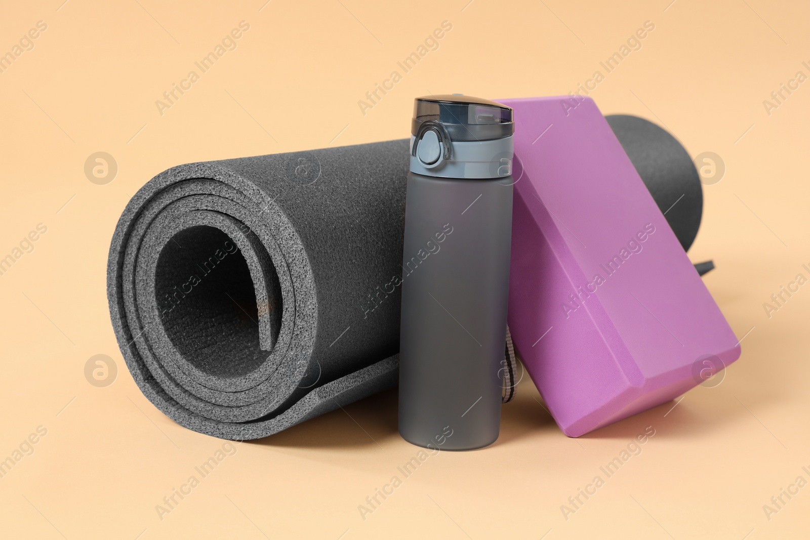 Photo of Grey exercise mat, yoga block and bottle of water on beige background