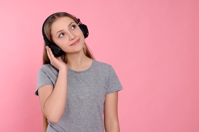 Photo of Teenage girl listening to music with headphones on pink background. Space for text