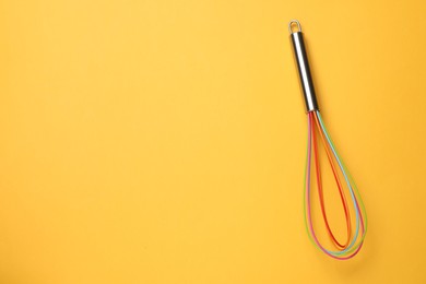 Bright whisk on yellow background, top view. Space for text