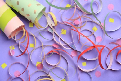 Photo of Beautiful serpentine and confetti bursting out of party poppers on violet background, flat lay